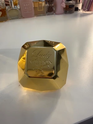 Lady Million parfymflaska - Snygg Lady Million parfym från Paco Rabanne med ikonisk guldfärgad design. Perfekt för dig som vill sticka ut och ge din samling en lyxig touch. 30 ml, ungefär halva kvar 