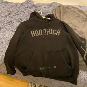 Svart HOODRICH hoodie med tryck - Svart hoodie från HOODRICH med stor logga framtill och tryck på ryggen. Köpt för 900 kr jd  använt i 5 månader ungefär andvänd fåtal gånger. Priset kan diskuteras vid snabb affär.
