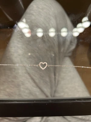 Silverarmband - Snyggt och tunt armband i äkta silver med ett glittrigt hjärta i mitten, dekorerat med små cubic zirconia-stenar. Justerbar längd med karbinlås och stämpel 925. Täcken på användning vid slutet av kedjan men annars i fint skick