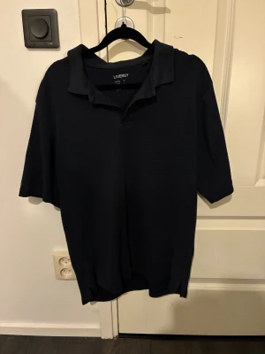 Mörkblå piké från Livergy - En stilren mörkblå pikétröja från Livergy med klassisk krage och korta ärmar. Tröjan är tillverkad i mjuk bomull och har en enkel, tidlös design utan mönster eller tryck. Perfekt för en clean och avslappnad look.