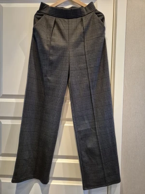 Grå-rutiga kostymbyxor från H&M - Snygga grå kostymbyxor från H&M med klassiskt rutigt mönster. Byxorna har en rak och lite vidare passform, hög midja och pressveck framtill.