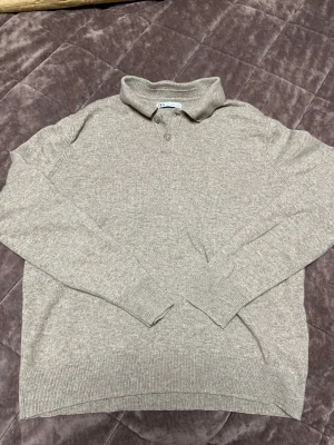 Beige stickad pikétröja från ZARA - Säljer en beige stickad pikétröja från ZARA med klassisk krage och två knappar framtill. Tröjan har långärmad design och ribbade muddar vid ärmslut och nederkant. Perfekt för dig som gillar stilrena och enkla plagg med en chill vibe.