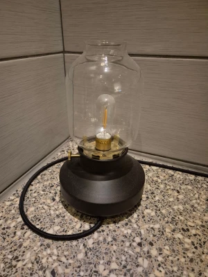 Elektrisk bordlampa med glaskupa - Stilren elektrisk bordlampa med rund svart fot, mässingsdetaljer och glaskupa. Lampan har en synlig LED-ljuskälla och tygklädd sladd. Inga synliga defekter eller slitage, passar perfekt som dekorativ belysning i hemmet. Helt nya 2 st för 350 kr för båda.