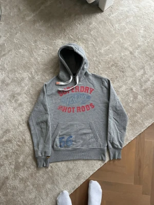 Superdry hoodie - Väldigt snygg och eftertraktad Superdry hoodie med riktigt coolt tryck och skön passform. Skick:7,5/10 skriv gärna med minsta fråga eller om fler bilder! 