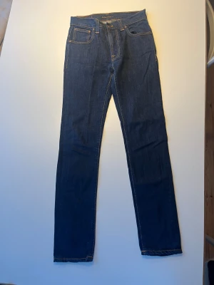Mörkblå jeans från Nudie Jeans - Säljer ett par mörkblå jeans från Nudie Jeans med klassisk femficksdesign och kontrastsömmar. Modell Thin Finn, utan slitningar. Mycket fint skick. 29/32