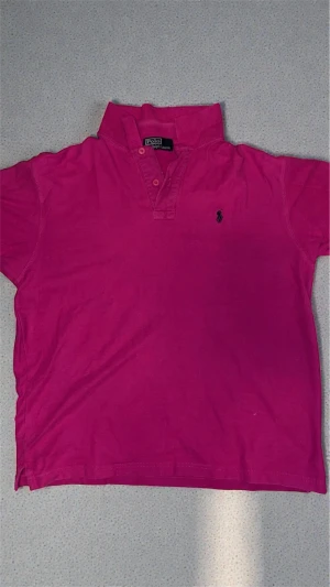 Rosa pikétröja från Polo Ralph Lauren - Säljer en snygg rosa pikétröja från Polo Ralph Lauren med klassisk krage och knappslå. Tröjan har korta ärmar och den ikoniska logon broderad på bröstet. Perfekt för dig som vill ha en färgstark och stilren look.