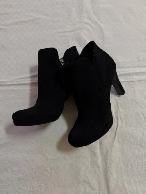 Svarta stövletter från Tamaris, storlek 39 - Snygga svarta stövletter från Tamaris i storlek 39. Skorna har en rund tå, hög klack och är gjorda i mjuk mocka. De har dragkedja på sidan för enkel på- och avtagning. Perfekta för dig som gillar stilrena och klassiska boots med lite edge.