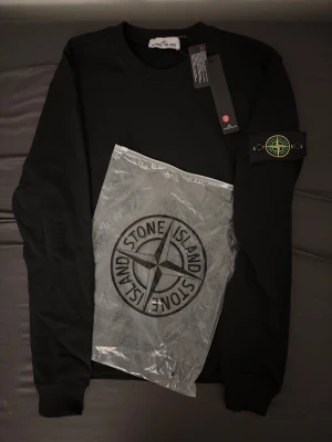 Stone Island sweatshirt M - Svart sweatshirt från Stone Island i storlek M. Klassisk rund hals och ribbade muddar. Ikonisk patch med logga på vänster ärm, fäst med knappar. Tröjan är tillverkad i mjuk bomull och har en clean, stilren look som är lätt att matcha med jeans eller cargo. Aldrig använt helt ny, pris kan diskuteras!