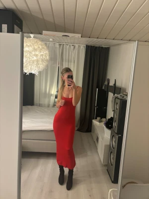 Röd långklänning med smala axelband - Säljer en snygg röd långklänning med smala axelband och figurnära passform. Klänningen är ärmlös och har en enkel, stilren design som framhäver siluetten. Stretchigt matrial