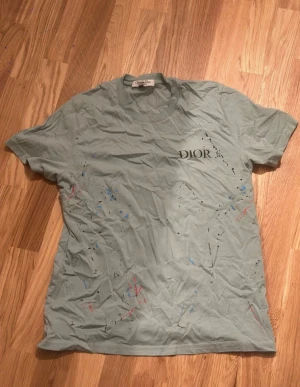 Ljusblå t-shirt med färgstänk - Färgstänk i blått, svart och rött. Klassisk rund hals och korta ärmar. T-shirten är i mjuk bomull och har loggan tryckt på bröstet. Perfekt för dig som gillar streetstyle och exklusiva märken.