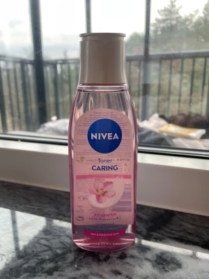 NIVEA Caring Toner med mandelolja - NIVEA Caring Toner är en ansiktsvatten med mandelolja och Hydramine, perfekt för torr och känslig hud. Kommer i en genomskinlig rosa plastflaska med vitt lock och rymmer 200 ml. Formulan är vegansk och flaskan är tillverkad av återvunnen plast.