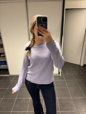 Ljuslila stickad tröja med rund hals - Säljer en ljuslila stickad tröja med rundad hals och långa ärmar. Tröjan har ribbade muddar vid ärmslut och nederkant, vilket ger en snygg och enkel look. Perfekt att matcha med jeans eller kjol för en chill stil.