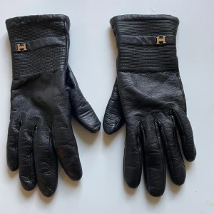 Svarta skinnhandskar från Hollies XS - Svarta skinnhandskar från Hollies i storlek XS (6). Handskarna har ett diskret H-emblem i metall vid handleden och ribbade detaljer upptill. Insidan är fodrad i mjukt material för extra värme. Perfekta för kalla dagar när du vill ha en stilren look.