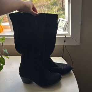 Svarta mockastövlar med klack - Säljer ett par svarta stövlar i mocka med rund tå och låg klack. Stövlarna har dragkedja på insidan och en klassisk, enkel design som funkar till många outfits. Perfekta för höst och vinter när du vill ha en stilren look.