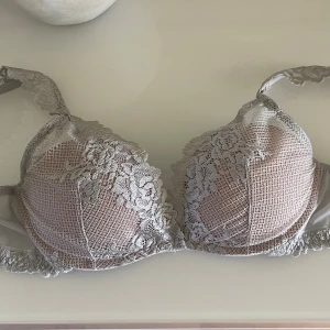 Grå spets-bh från Intimissimi - Säljer en snygg grå bh från Intimissimi med vacker spets och blommigt mönster. Bh:n har vadderade kupor och justerbara axelband, perfekt för dig som gillar en feminin och stilren look. Endast testad.