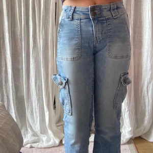 Blå cargojeans från Lindex Freja - Säljer ett par ljusblå cargojeans från Lindex Freja med stora fickor på benen och snygga sömdetaljer. Jeansen har hög midja, raka ben och stängs med dubbla knappar. Perfekta för en chill och trendig look. ✨💞✨