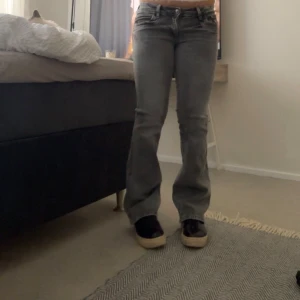 Grå bootcut jeans med låg midja - Säljer ett par grå jeans med bootcut-modell och låg midja. Jeansen har klassiska fem fickor, dragkedja och knapp framtill. Snygg tvätt och skön passform som ger en retrovibe. Perfekta till sneakers eller boots.