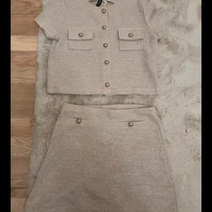 Beige stickad kjol och topp med knappar från H&M - Snygg beige stickad kjol och topp med dekorativa knappar framtill och fickdetaljer.
