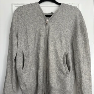 Grå hoodie i merinoull/kashmir S&T - Mysig ljusgrå hoodie från S&T Clothing i en lyxig blandning av merinoull och kashmir. Har ett litet hål vid lappen och armbågen 