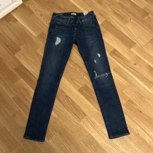Hilfiger Denim skinny jeans blå 26/30 - Mörkblå skinny jeans från Hilfiger Denim med slitningar och distressed detaljer på benen. Klassisk femficksmodell med låg midja och smal passform. Snygga kontrastsömmar och Hilfiger-logga på bakfickan. Perfekta för en avslappnad streetstyle.
