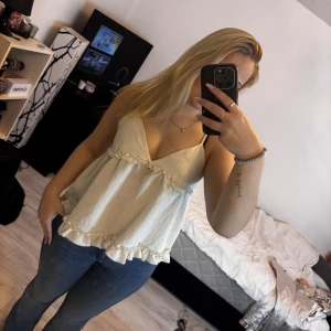 Vita volangtop med smala axelband - Supersöt vit linnetopp med volangdetaljer och smala axelband. Toppen har v-ringning och en flowy passform som ger en luftig känsla. Perfekt för varma dagar och enkel att styla med jeans eller kjol.