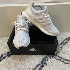 Adidas Ultraboost vita sneakers - Säljer ett par fräscha Adidas Ultraboost sneakers i helvitt. Skorna har stickad ovandel i syntet, klassiska tre ränder på sidan och snörning. Boost-sulan ger grym komfort och dämpning. Perfekta för dig som gillar stilrena och sportiga sneakers.