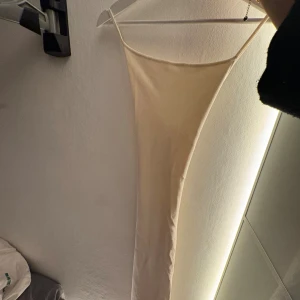 Champagnefärgad långklänning Gina Tricot - Supersnygg långklänning från Gina Tricot i champagnefärgat ribbat material. Klänningen har smala axelband, figurnära passform och öppen rygg med snygga banddetaljer. Perfekt för dig som vill sticka ut med en stilren och trendig look.