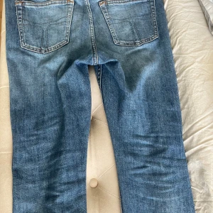 Blå jeans från Tiger of Sweden - Snygga blå jeans från Tiger of Sweden med klassisk femficksdesign och kontrastsömmar. Jeansen har rak passform och normal midja, tillverkade i slitstarkt denimtyg. Perfekta för dig som gillar en tidlös och clean look.
