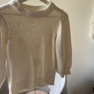 Vit stickad tröja från Gina Tricot - Superfin vit stickad tröja från Gina Tricot med puffiga ärmar och bred ribbad kant vid hals, ärmslut och nederkant. Perfekt för lager på lager och passar till allt. Mjuk och skön, enkel att styla till jeans eller kjol.