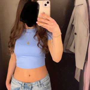 Ljusblå croppad topp - Säljer en ljusblå croppad topp med korta ärmar. Toppen har en tight passform och är tillverkad i ett mjukt, stretchigt material som sitter snyggt på kroppen. Perfekt att matcha med jeans