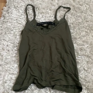 Olivgrön linnetopp med spets från 157 - Snygg olivgrön linnetopp från 157 med tunna axelband och v-ringning dekorerad med spetsdetaljer. 