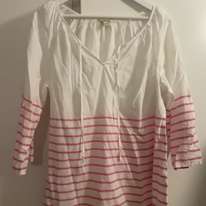 Vit och rosa randig blus/tunika, XL - Snygg vit blus från G.H. Bass & Co. i storlek XL med rosa horisontella ränder nedtill och på ärmarna. Klänningen har v-ringning med snörning och trekvartsärmar. Tillverkad i 100% bomull.