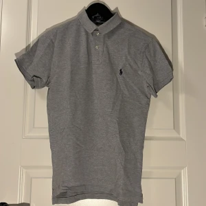 Grå pikétröja Ralph Lauren - Klassisk grå pikétröja från Polo Ralph Lauren  mycket stilren och snygg. Är i storlek M men sitter mer som S. Passar på mellan 170-180. Mycket bra skick, inget synligt tecken på användning. Självklart äkta, hör av er vid minsta fundering eller om ni vill ha fler bilder! Kollar gärna in min profil för fler snygga plagg⭐️