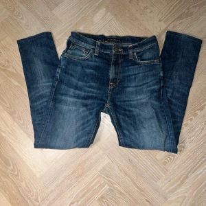 Mörkblå jeans från Nudie Jeans Co W30 L34 - Säljer ett par mörkblå jeans från Nudie Jeans Co i klassisk femficksmodell. Jeansen har orange kontrastsömmar och raka ben. Tillverkade i slitstarkt denimtyg av bomull. Perfekta för dig som gillar en tidlös och clean look.