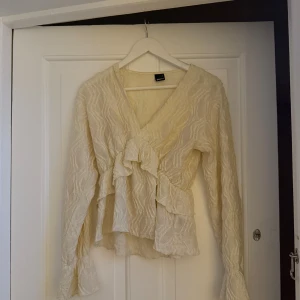 Beige omlottblus med volanger Gina Tricot - Supersöt beige omlottblus från Gina Tricot i storlek S med v-ringning, långa ärmar och volangdetaljer framtill. Säljer då den inte kommer till användning.🤍