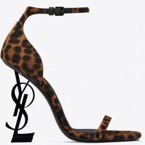 YSL sandaler med logoklack - Säljer ikoniska sandaler från Saint Laurent med YSL-logga som klack. Finns i leopardmönstrad mocka, vit och guld skinn, samt röd lack. Alla har smal rem över tårna, ankelrem med spänne och spetsig tå. Perfekt statement piece för dig som vill sticka ut.