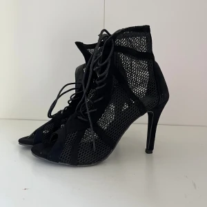 Svarta Pumps med Höga Klackar  - Säljer ett par svarta pumps med höga klackar och coolt nätmaterial. Skorna har snörning framtill och öppen tå. Materialet är en mix av mocka och syntet med meshdetaljer perfekta för att dansa. Danskorz