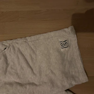 Grå sweatshorts från Gant - Säljer ett par ljusgrå sweatshorts från Gant med GANT USA-logga på benet. Shortsen har snörning i midjan och är tillverkade i mjuk bomullsmix, perfekta för chill dagar eller träning. Klassisk och avslappnad passform med fickor på sidorna.