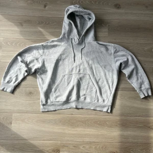 Grå hoodie från Weekday i bomull - Säljer en ljusgrå hoodie från Weekday i storlek S. Tröjan har huva med snörning, magficka och ribbade muddar. Tillverkad i mjuk bomullsmix, perfekt för chill dagar. Klassisk och enkel design som funkar året runt.