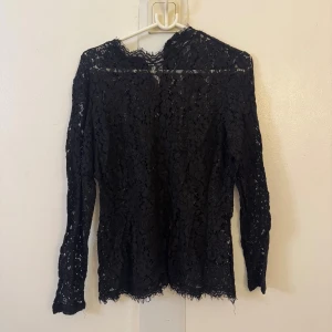 Svart spetsblus med lång ärm - Säljer en svart blus i spets med lång ärm och hög hals. Blusen har ett vackert blommigt spetsmönster och råa kanter vid hals och nederkant. Perfekt för dig som vill ha en elegant och trendig look. Passar S-L beroende på hur tajt man vill ha den!