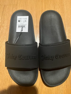 Juicy Couture tofflor  - Säljer ett par helt nya och oanvända Juicy Couture Breanna Embossed Slider Black i storlek EU 39. Ordinarie pris: 500kr