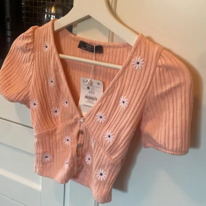Sommar topp - Fin aprikos rosa topp med blommor och knappar från bershka . Har aldrig använts. Skriv om ni har några övriga frågor