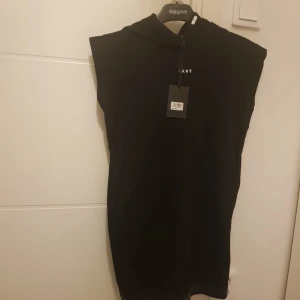 Dkny ny klänning 12 år - Fin ny, oanvänd klänning märke DKNY. Klänning är för 12 år gammal tjej, men jag tycker kan användas i och med till ålder 13 och 14. Svart, utan armar och med luva.