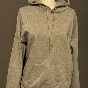 Grå hoodie - Säljer en supermysig grå hoodie. Den är perfekt för kalla dagar och har en stor ficka på magen samt en justerbar huva med snören. Den är långärmad och gjord av mjukt material som känns skönt mot huden. Perfekt för både chill och vardag!