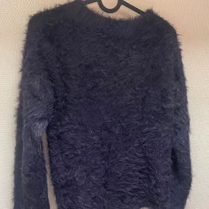 Mörkgrå fluffig tröja från H&M - En mjuk och bekväm mörkblå fluffig tröja från H&M. Tröjan har långa ärmar och en rund halsringning.