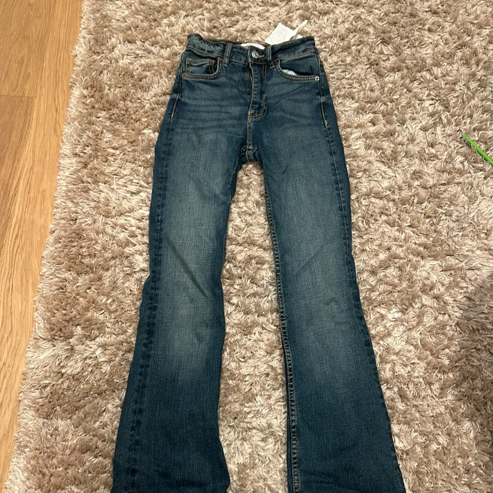 Säljer ett par snygga blå jeans från ZARA i storlek 32. De är i bra skick och har en klassisk femficksdesign med dragkedja och knapp framtill. Jeansen har en bootcut-stil som ger en skön och avslappnad look. Perfekta för både vardag och fest!. Jeans & Byxor.