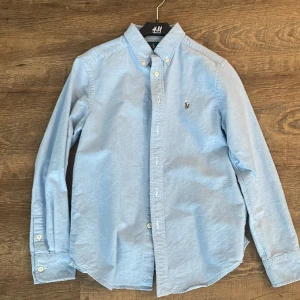 Ralph lauren skjorta - Detta är en ljusblå Ralph lauren skjorta som är i storlek barn medium eller till personer som är 10-12 år. 