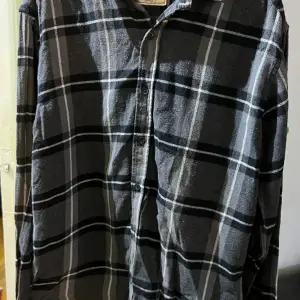 Rutig svart/grå flannelskjorta från these glory days i storlek L. Jättefint skick. Två extra knappar medföljes. Normal i storleken 