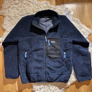 Patagonia Fleece Jacket - Introducing a sophisticated dark blue Patagonia fleece jacket in outstanding 9/10 condition. This timeless outerwear piece not only offers exceptional warmth but also elevates your style with its rich, deep hue. 