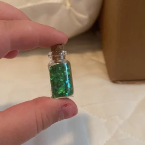 Litet glasflaska med grönt glitter - En liten glasflaska fylld med grönt glitter och försluten med en kork. Perfekt för dekoration eller hantverk.